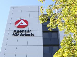 Agentur für Arbeit - Außenansicht mit Logo der AfA und einem Baum an einem sonnigen Tag