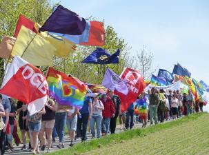 Demozug zum Ostermarsch - Eine Gruppe von Menschen geht auf einem Weg und trägt verschiedene Flaggen, darunter Regenbogen- und politische Fahnen. - FrieKoop | flickr - CC BY-NC 2.0