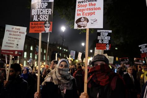 Viele Menschen stehen in der kalten Nacht und protestieren mit Transparenten und Plakaten gegen die Unterdrückung in Ägypten. Im Vordergrund sind zwei Frauen zu sehen, die ihre Gesichter verbergen.