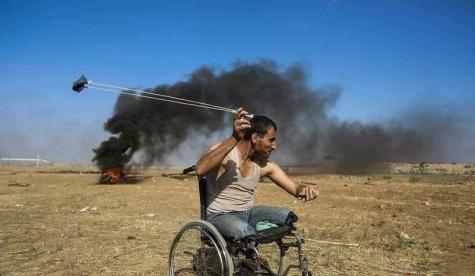 Ein Mann aus dem Gaza sitzt in einem Rollstuhl und bedient eine Steinschleuder