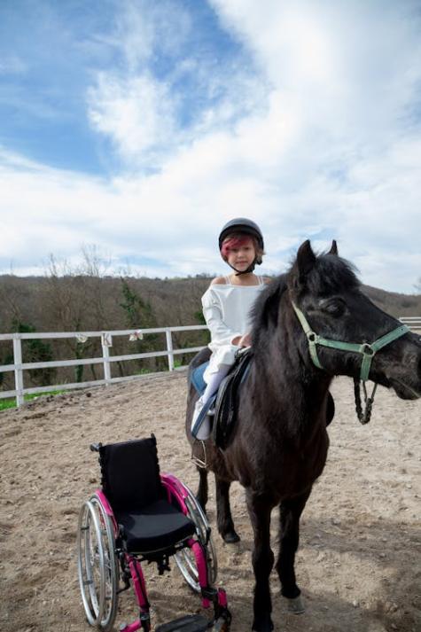 Gelähmtes Kind auf einem Pferd mit Rollstuhl daneben
