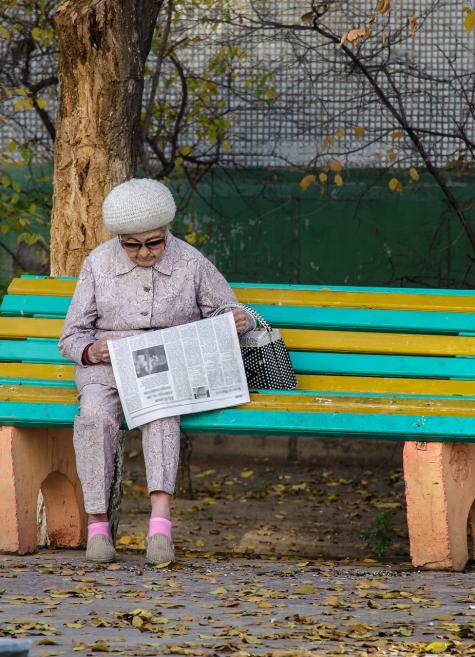 Seniorin liest Zeitung auf einer Bank